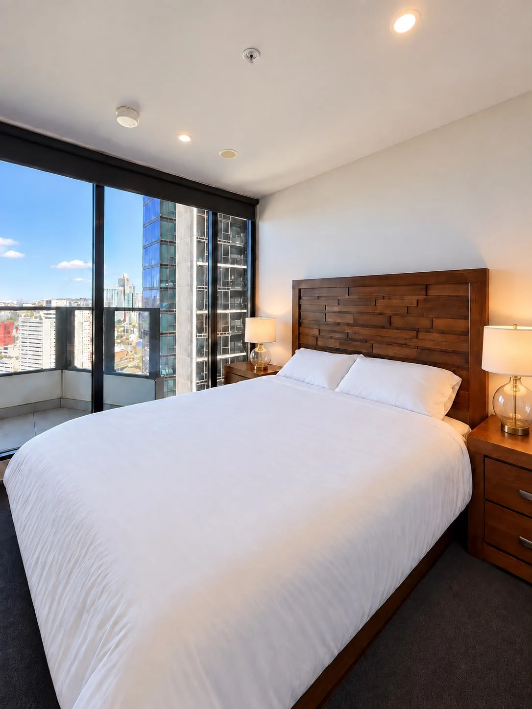 Bedroom with white bedding, a timber headboard and city views