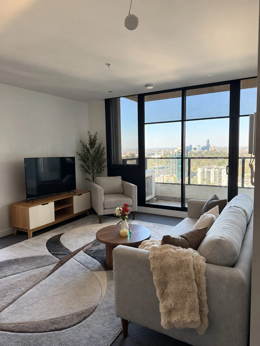Sunlit TV lounge with sofa and floor-to-ceiling windows overlooking Melbourne